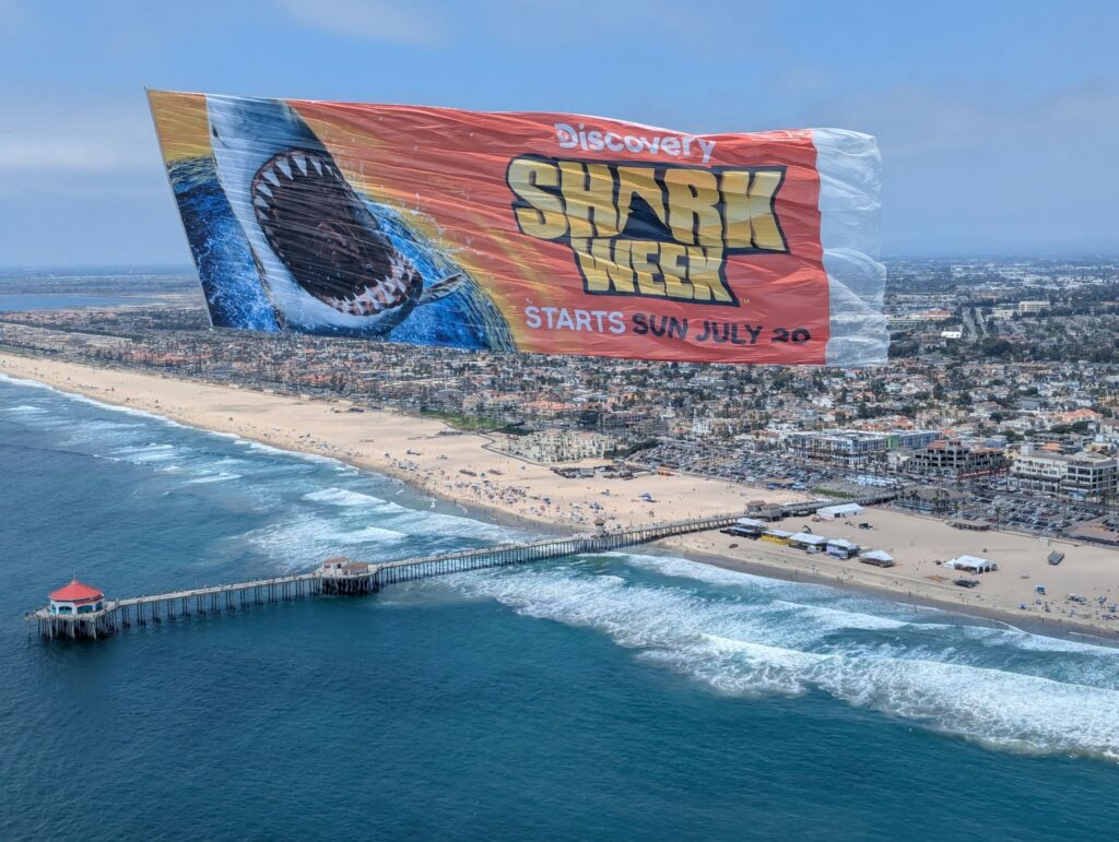 Full-color printed billboard banner flying over a beach and pier